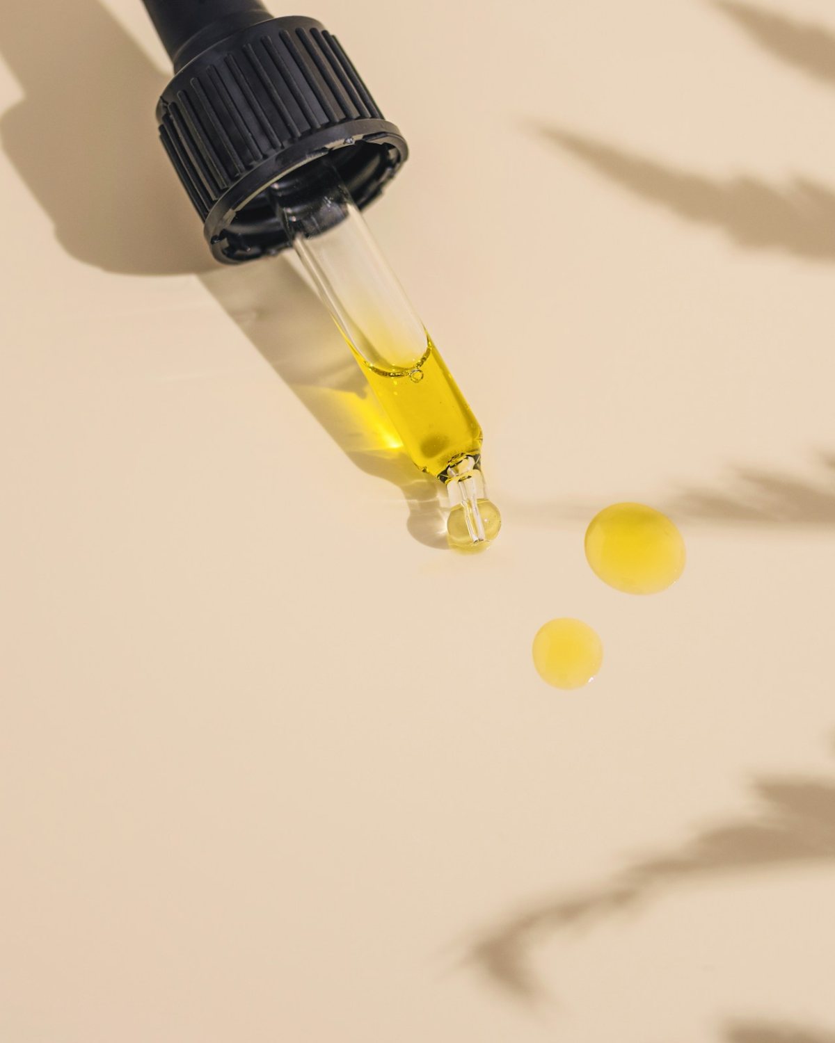 Golden oil dropping from a pipette in soft palm-leaf shadow