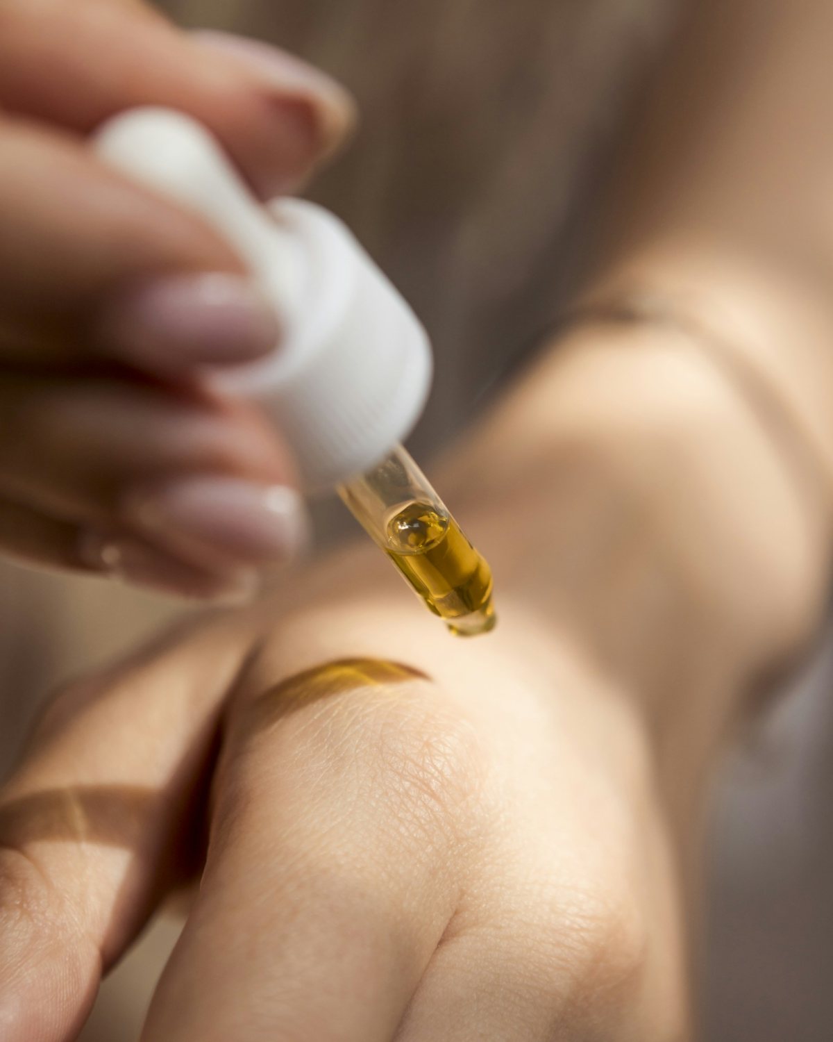 A drop of golden oil from a dropper onto the back of a hand