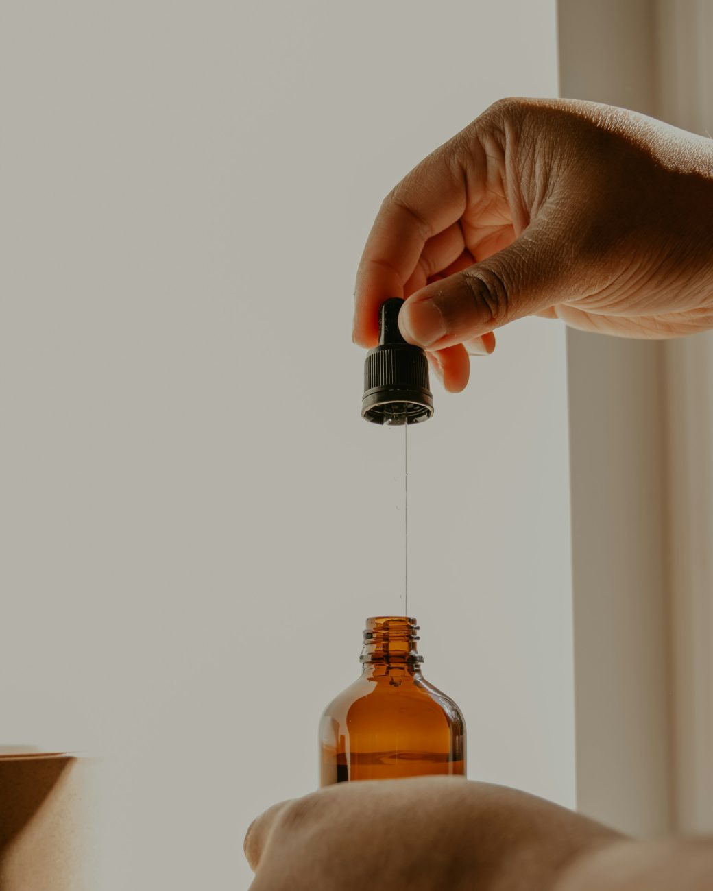 A hand lifting a glass dropper of oil out of an amber bottle