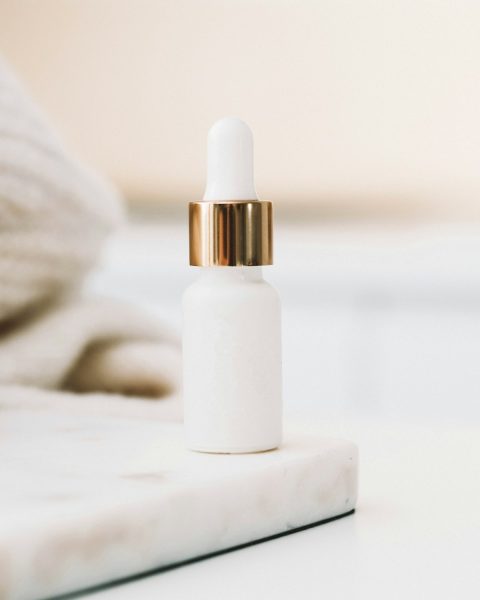 White dropper bottle with a gold collar on a marble tray