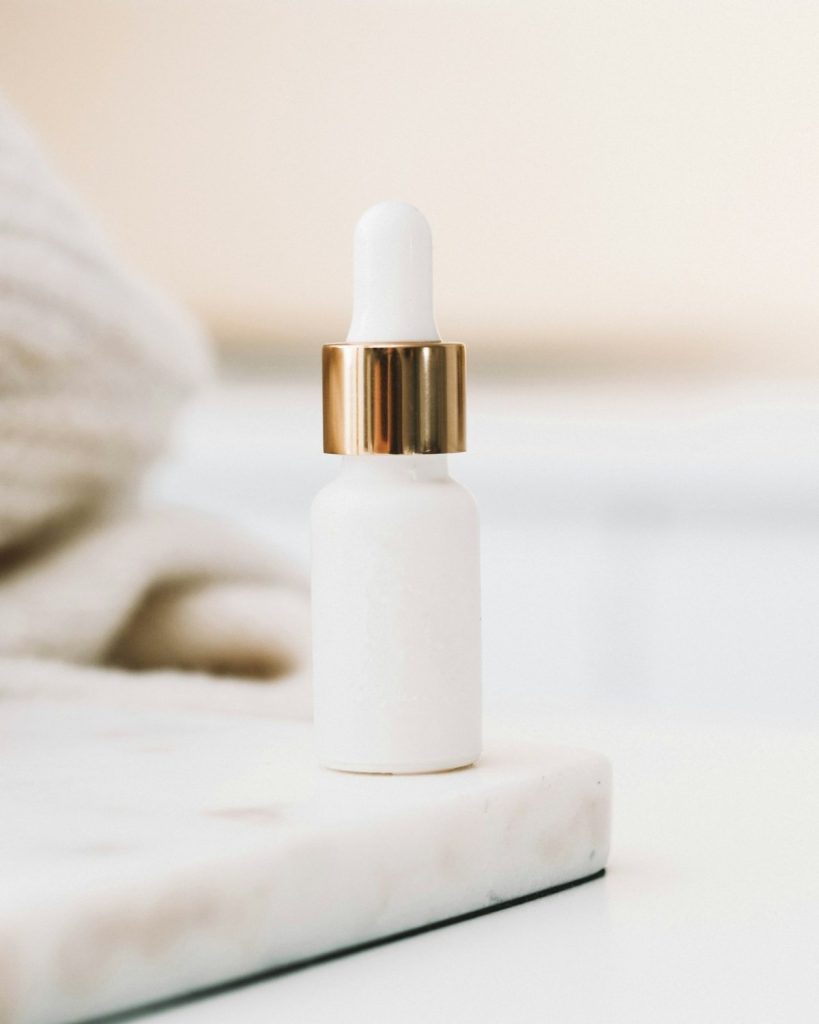 White dropper bottle with a gold collar on a marble tray