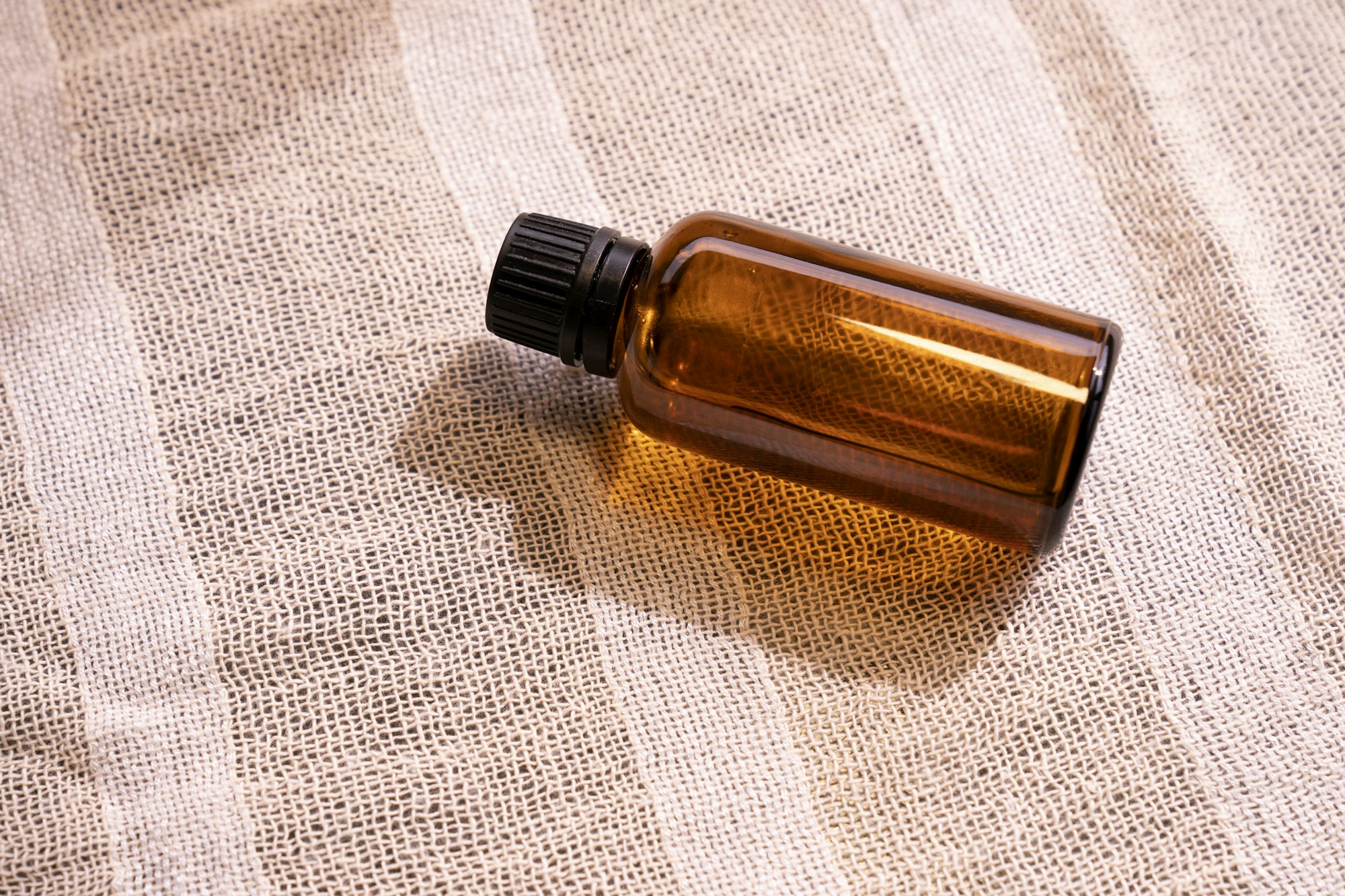 An unlabelled amber glass bottle lying on striped linen An unlabelled amber glass bottle lying on striped linen