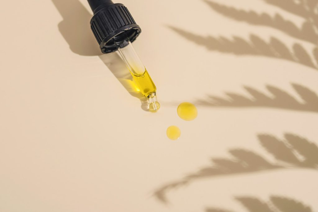 Golden oil dripping from a glass dropper onto a cream surface