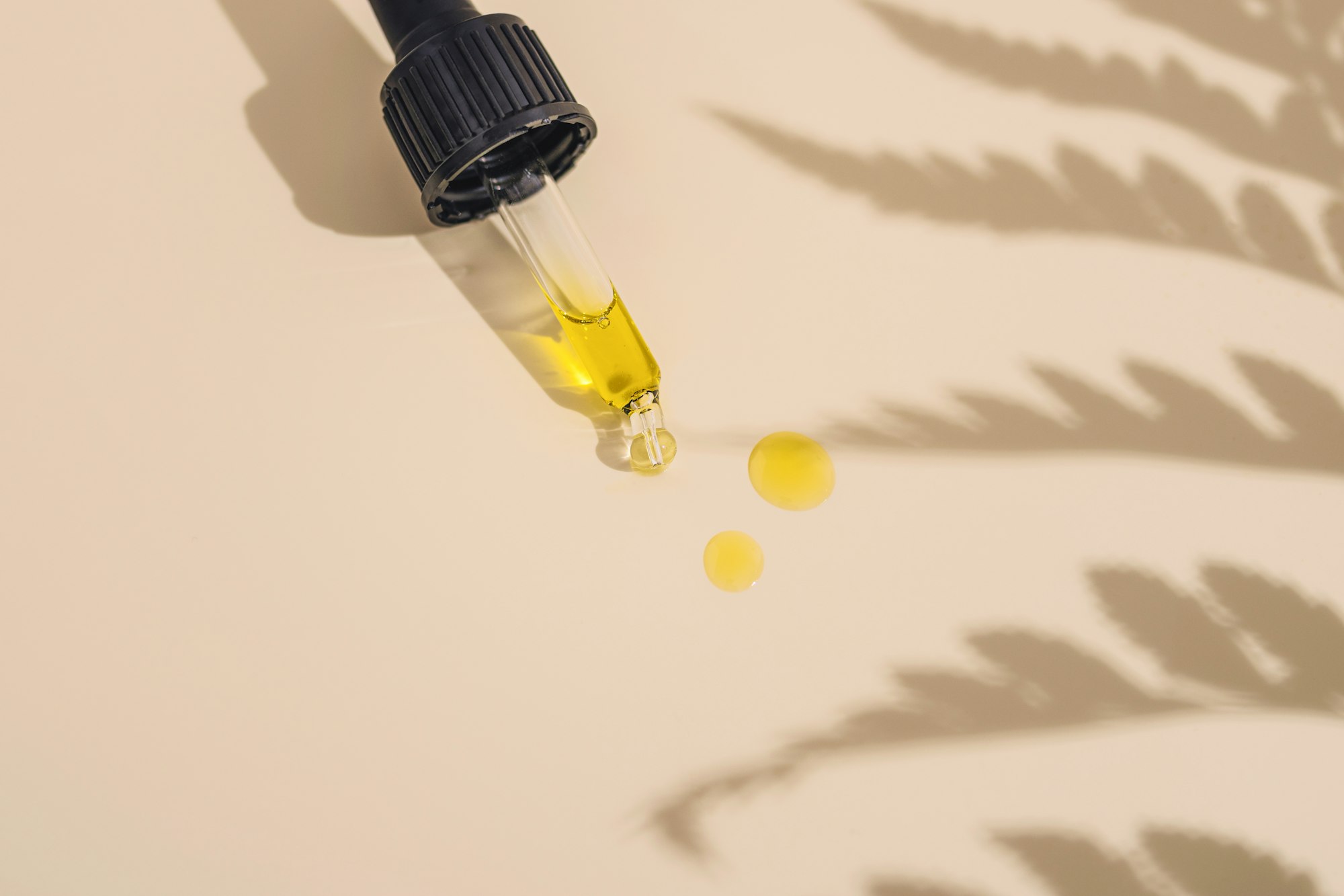 Golden oil dripping from a glass dropper onto a cream surface Golden oil dripping from a glass dropper onto a cream surface