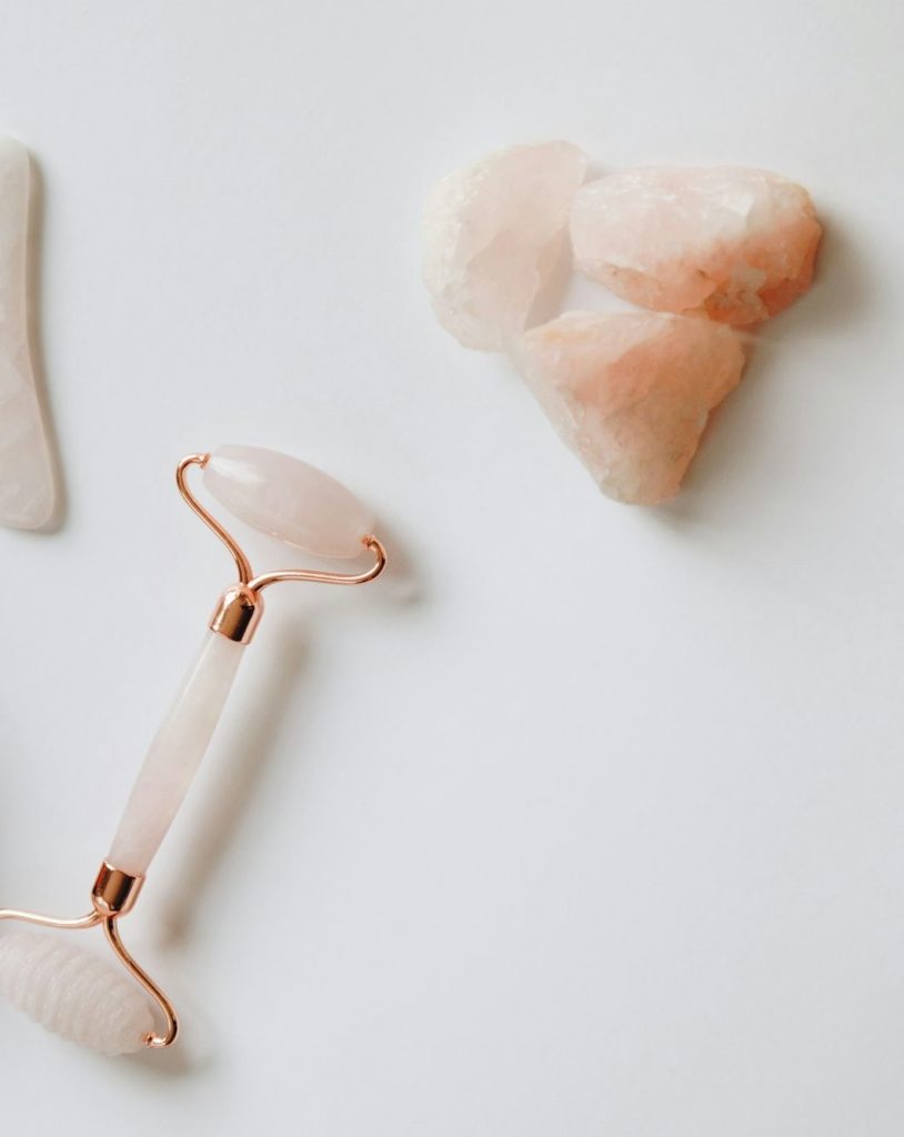 A rose quartz face roller, a gua sha stone and pieces of rose quartz on white