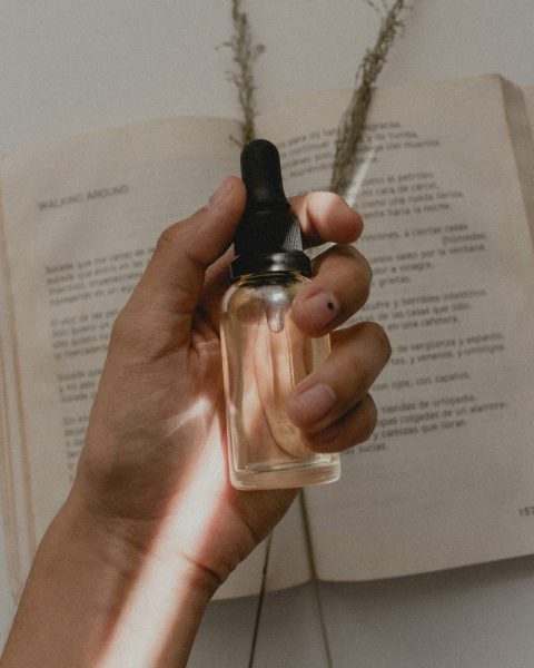 Hand holding a clear dropper bottle over an open book and dried grasses