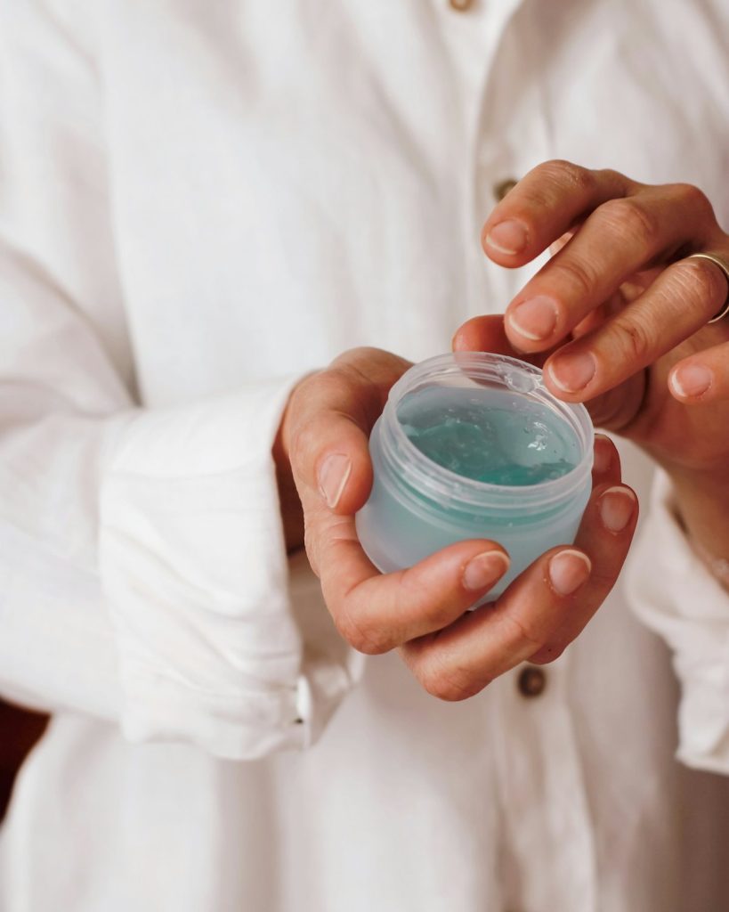 Hands opening a small jar of balm against a white linen shirt