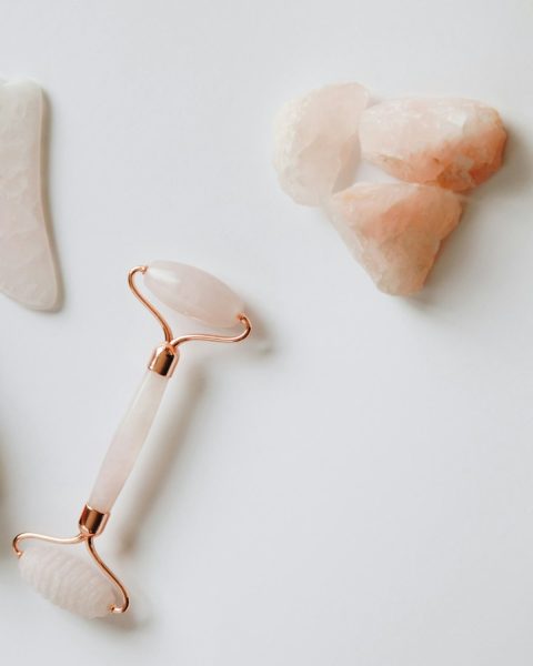 Rose quartz facial roller, gua sha stone and raw rose quartz on white