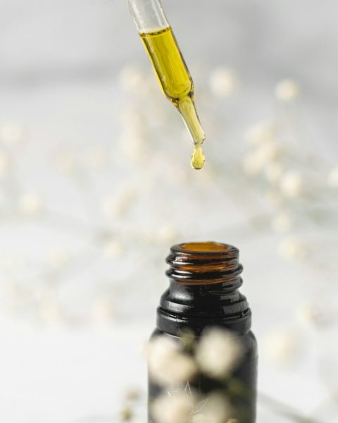 Golden facial oil dripping from a glass dropper into a small amber bottle
