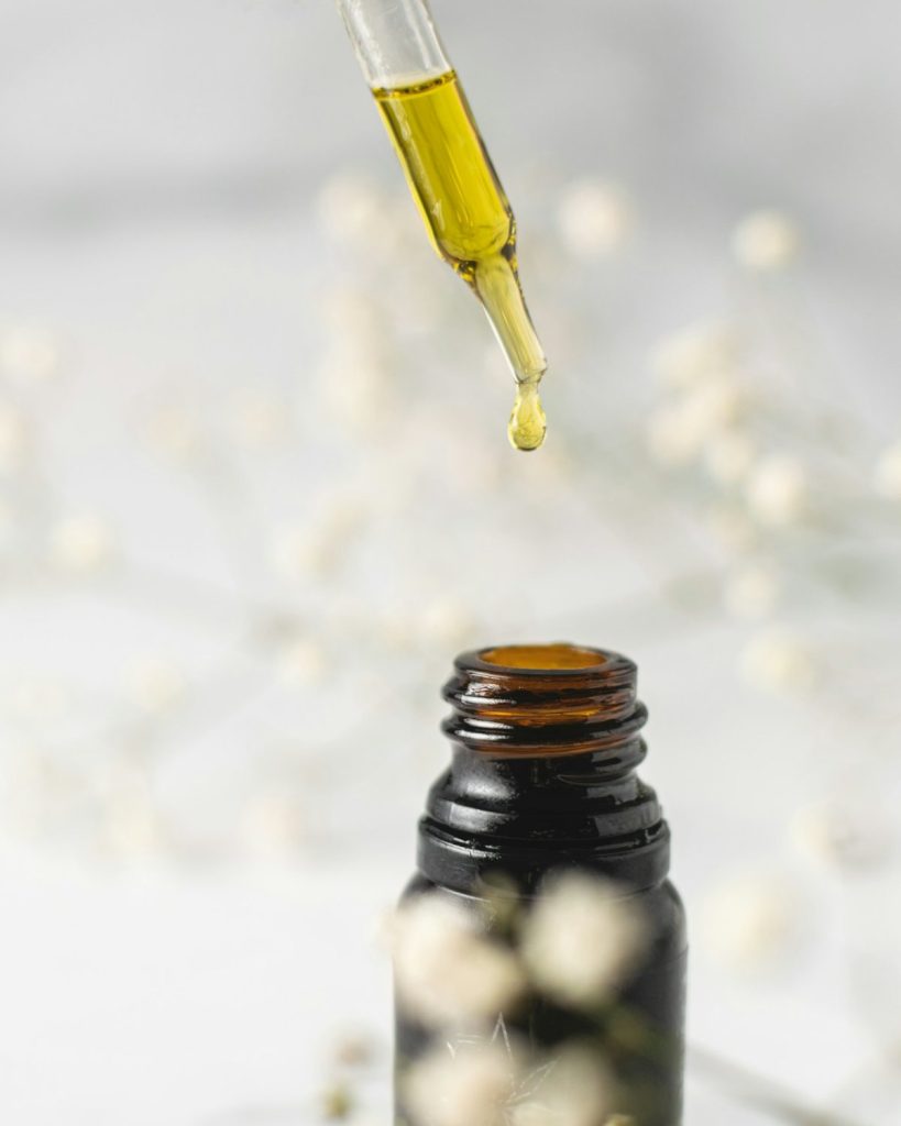 Golden facial oil dripping from a glass dropper into a small amber bottle